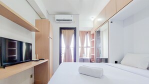 Une chambre d’hôtel moderne dotée d’une télévision à écran plat, d’un lit avec du linge de maison blanc, d’un système de climatisation intégré et d’une étagère en bois.