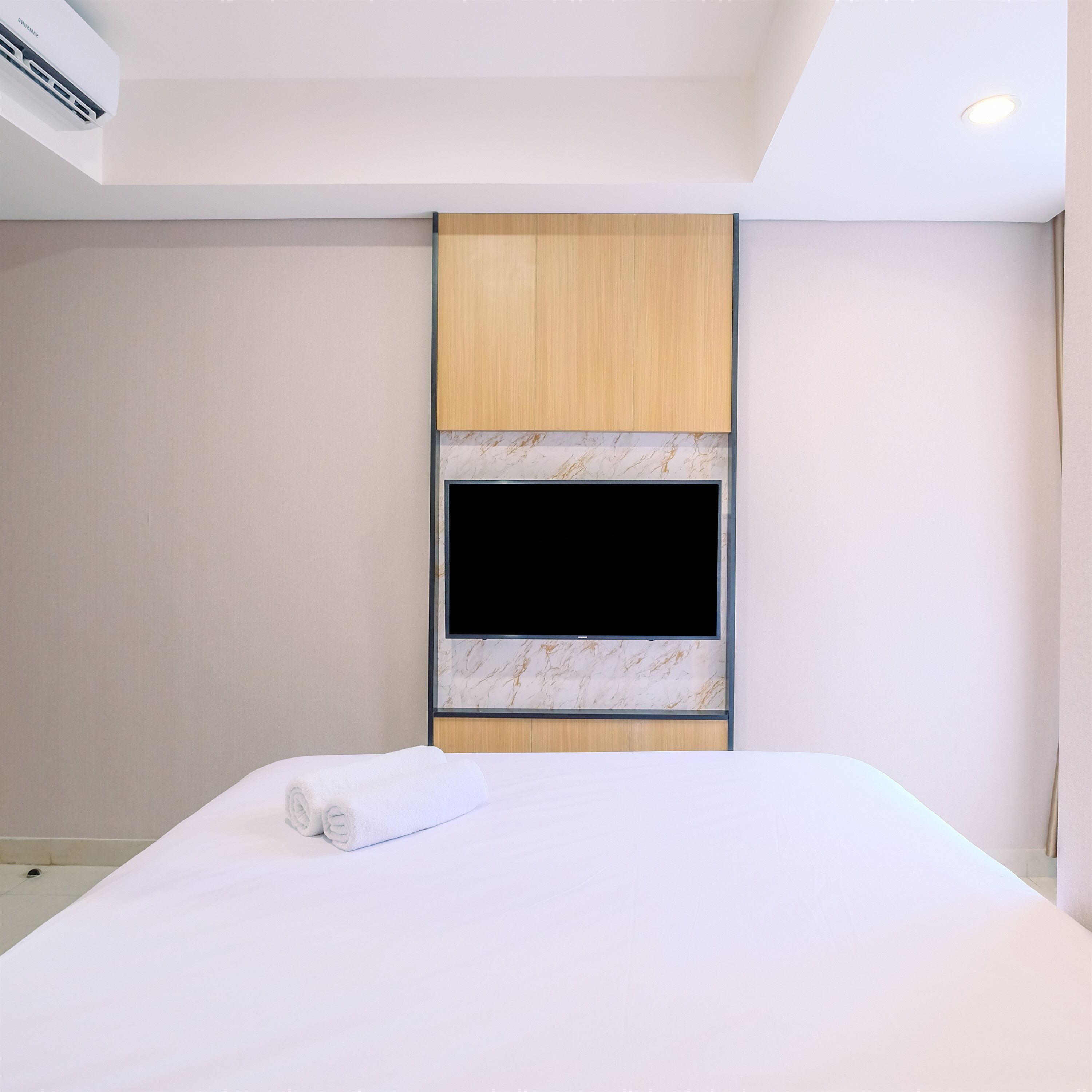 A modern hotel room with a large bed, a flat-screen TV mounted on a wooden panel, and a ceiling air conditioner.