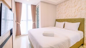A hotel room with a large bed, a flat-screen TV mounted on the wall, and a window with curtains.
