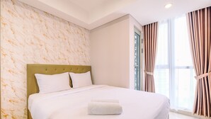 A neatly made bed with white linens and a folded towel, a headboard, and a window with curtains. - Comfort And Modern 1Br At Gold Coast Apartment (Jakarta)