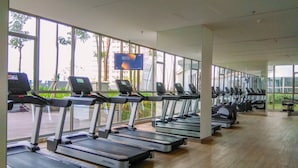 A gym with multiple treadmills aligned in rows, large windows, and a flat-screen TV mounted on the wall. - Comfort And Modern 1Br At Gold Coast Apartment (Jakarta)