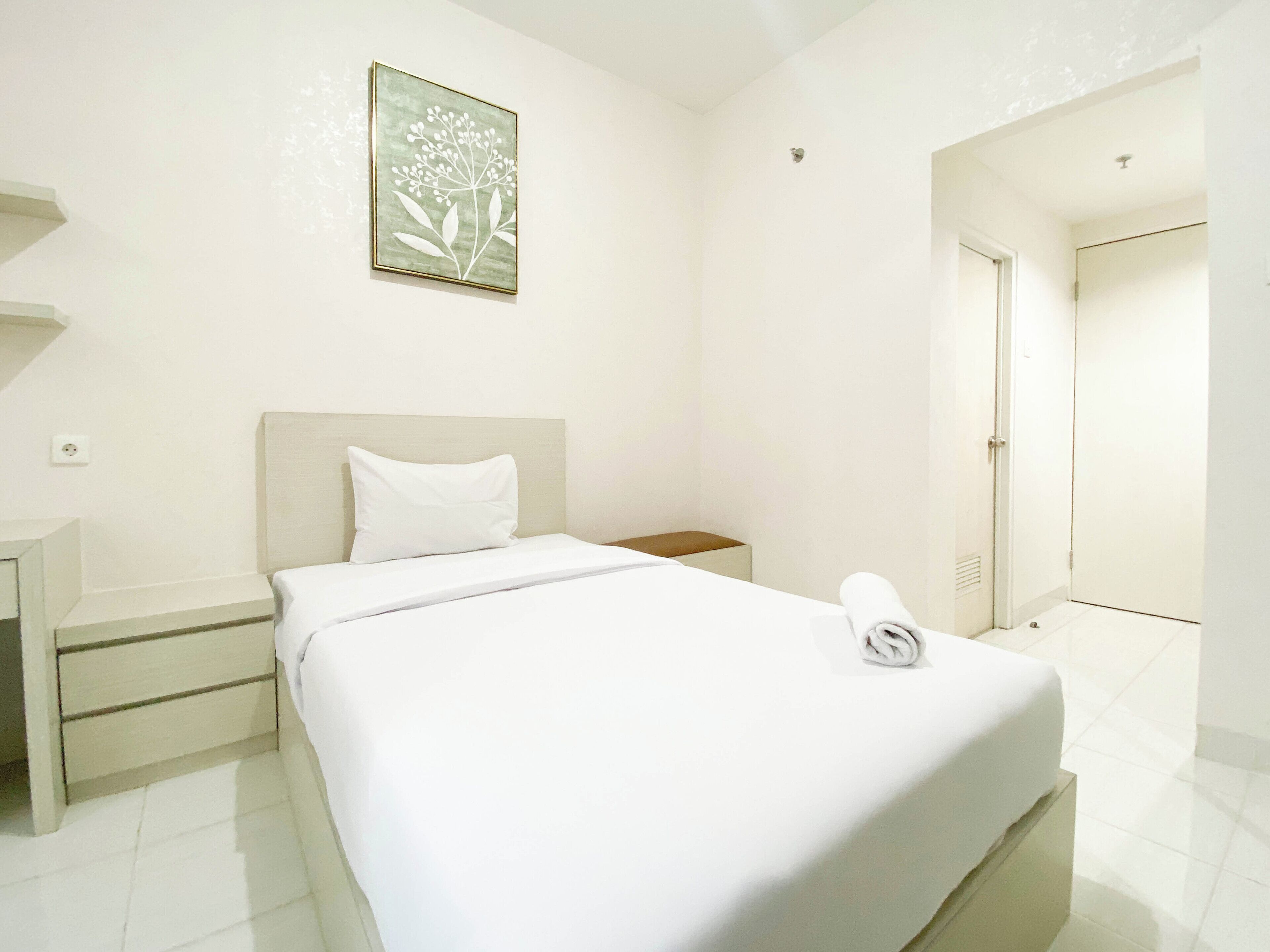 Una habitación de hotel con cama, mesita de noche, un cuadro en la pared y una puerta que da a otra habitación.