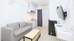 Um espaço de estar compacto com sofá, uma mesa pequena, cozinha compacta e televisão na parede.