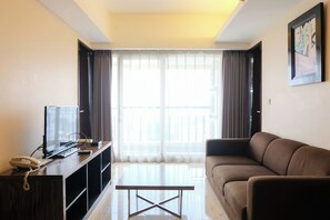 A living room with a sofa, a coffee table, a TV, and a phone on a wooden cabinet. - Good Choice 2Br Apartment At Braga City Walk (Bandung)