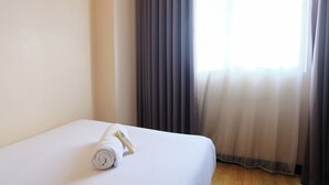Ett hotellrum med en snyggt bäddad säng, en hoprullad vit handduk och en fjärrkontroll på sängen.