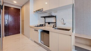 A modern kitchen with a built-in dishwasher, a stainless steel sink, and a black hanging rack. - Gorgeous And Tidy Studio At Sky House Bsd Apartment (Pagedangan)