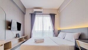 A hotel room with a bed, a TV, a desk, and a window with curtains. - Gorgeous And Tidy Studio At Sky House Bsd Apartment (Pagedangan)