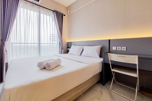 Una cama bien hecha con toallas enrolladas, una mesita de noche con lámpara y un estante en la pared.
