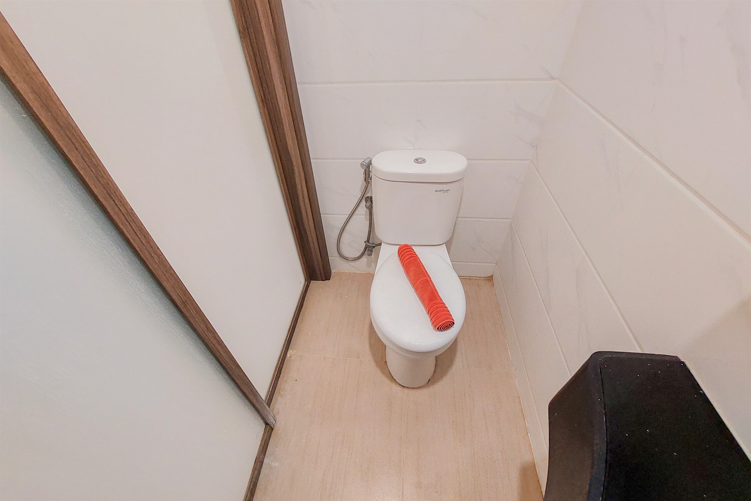 A small, clean bathroom with a white toilet, a wooden frame door, and a black trash bin.