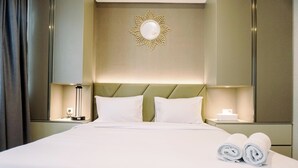 A hotel room with a large bed, two bedside tables, a wall-mounted light fixture, and a decorative sunburst mirror. - Homey And Cozy Studio Room Daan Mogot City Apartment (Jakarta)