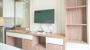 A modern room with a wooden desk, a flat-screen TV mounted on the wall, and a large mirror above the desk. - Comfort Living And Homey Studio Signature Park Grande Apartment (Jakarta)