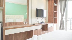 A modern hotel room with a large mirror, a flat-screen TV, a wooden vanity, and a balcony with a view. - Comfort Living And Homey Studio Signature Park Grande Apartment (Jakarta)