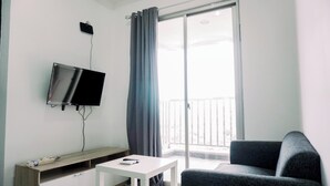 A modern living room with a flat-screen TV mounted on the wall, a white coffee table, a grey sofa, and a sliding glass door leading to a balcony. - Comfort And Homey 2Br Belmont Residence Puri Apartment (Jakarta)