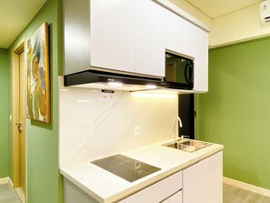Cozinha compacta com armários brancos, micro-ondas preto e pia de aço inoxidável.