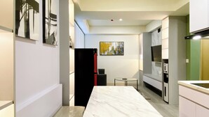 A modern kitchen with a marble countertop, a black refrigerator, and a small round table. - Best Homey 2Br At Meikarta Apartment (Cikarang)