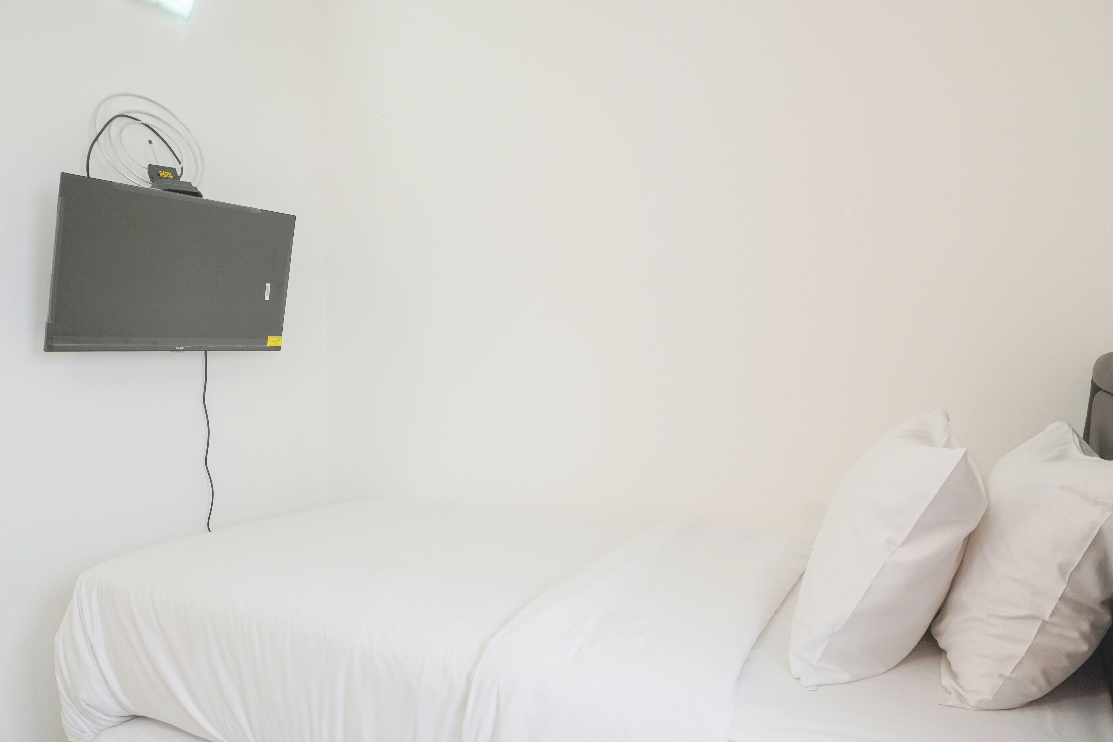 Un letto con biancheria bianca e due cuscini, una televisione montata a parete e un cavo di alimentazione.