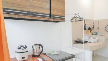 Una kitchenette compacta con un refrigerador pequeño, una tetera, una cocedora de arroz y una cafetera.