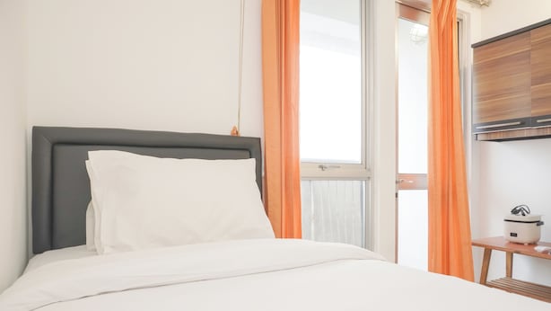 A neatly made bed with white linens, a grey headboard, and a small bedside table with a white kettle. - Minimalist Studio Taman Semanan Indah Cengkareng Apartment (Jakarta)