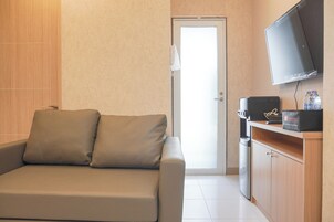 A modern hotel room with a sofa, a coffee machine, a TV, and a minibar.
