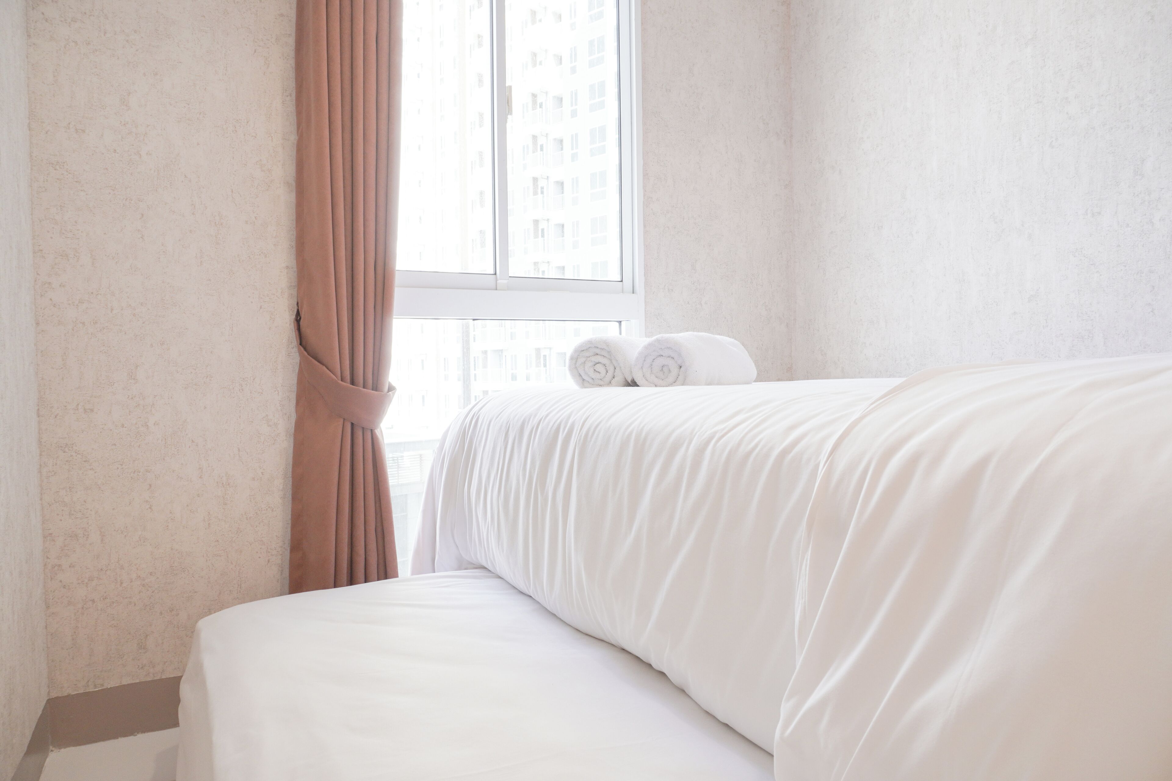 A hotel room with a bed, a window with curtains, and a view of buildings outside.