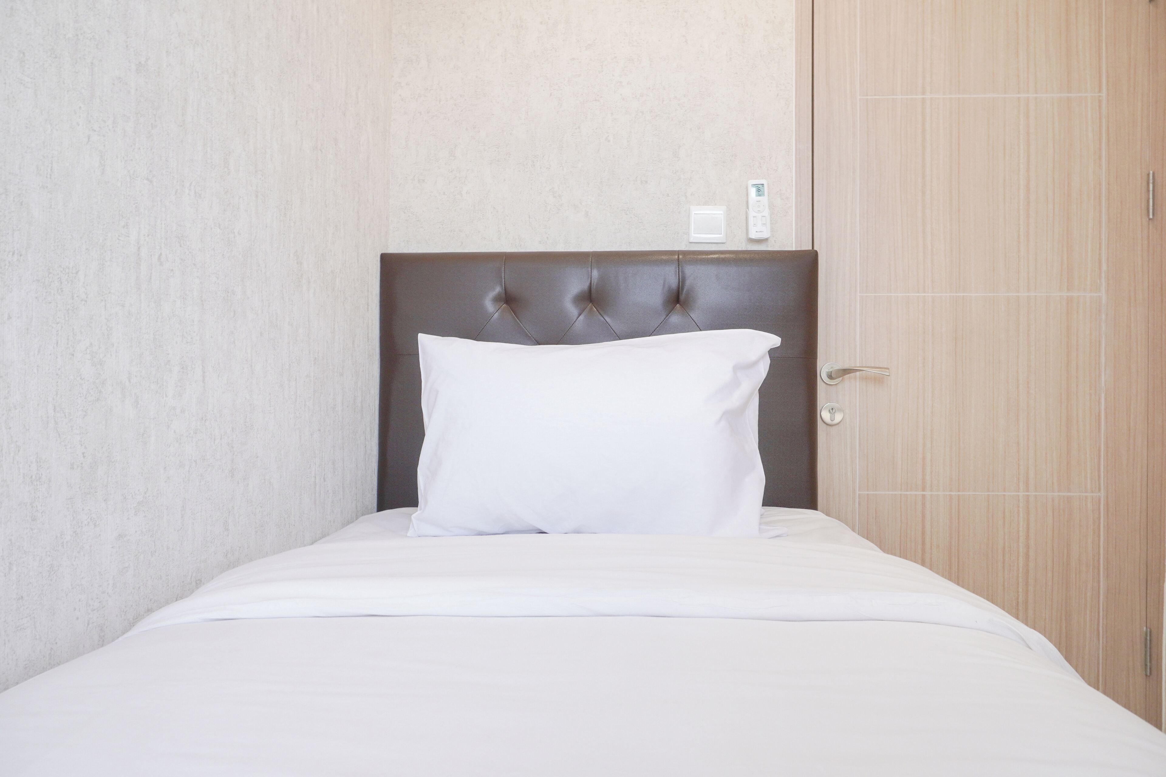 A neatly made bed with a white pillow and a brown headboard in a hotel room.