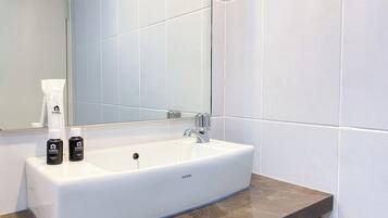 Un baño con lavamanos blanco, espejo y artículos de aseo.