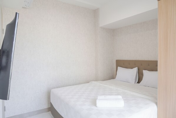 A hotel room with a bed, a flat-screen TV mounted on the wall, and a wooden headboard. - Homey 2Br At Tokyo Riverside Pik 2 Apartment (Teluknaga)