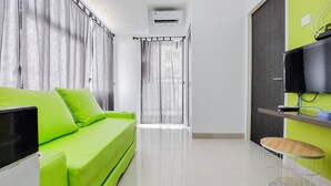 A modern living room with a green sofa, a flat-screen TV, a small wooden table, and a sliding door leading to another room. - Gorgeous And Homey 2Br Serpong Garden Apartment (Cisauk)