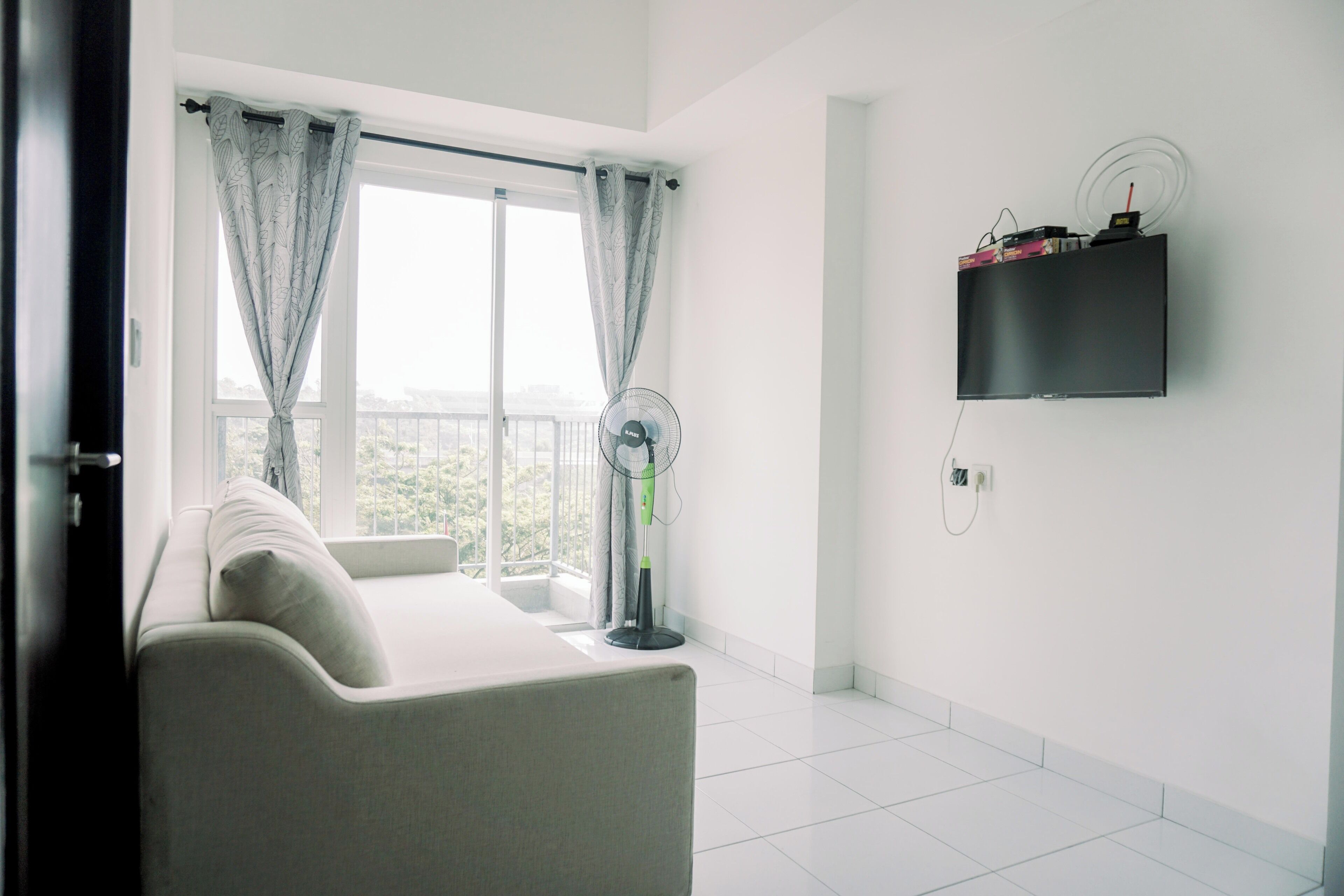 A modern room with a sofa, a standing fan, and a mounted TV.