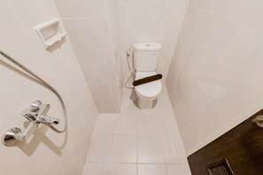 A bathroom with a white toilet, a shower with a handheld showerhead, and a wall-mounted faucet. - Minimalist And Homey Studio Serpong Garden Apartment (Cisauk)
