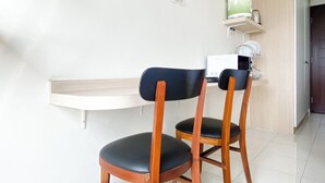 Une petite kitchenette équipée d’un four à micro-ondes, d’une machine à café et d’une étagère au-dessus du plan de travail. On y trouve deux chaises en bois avec des coussins noirs.