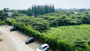 Un parking où sont garées plusieurs voitures, entouré d’une végétation luxuriante et d’arbres.