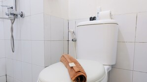 Eine weiße Toilette mit einem braunen Handtuch auf dem Sitz, einer Duschbrause und einem Toilettenpapierhalter.