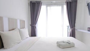 Ein Hotelzimmer mit einem großen Bett, weißer Bettwäsche und Blick ins Freie durch Vorhänge.