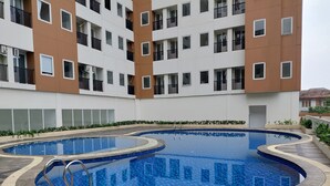 A swimming pool with a tiled edge, surrounded by a building with balconies and windows. - Cozy And Simply Studio Apartment At Urban Heights Residences (South Tangerang)
