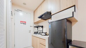 A compact kitchen with a stainless steel refrigerator, wooden cabinets, and a white countertop. - Cozy And Simply Studio Apartment At Urban Heights Residences (South Tangerang)