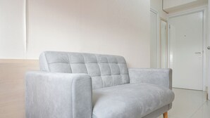 A light grey sofa with wooden legs in a room with white walls and a closed door in the background. - Good Deal 1Br Green Pramuka City Near Mall Apartment (Jakarta)