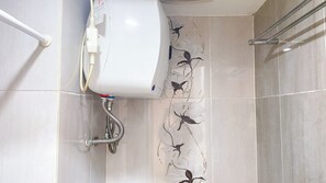 A bathroom with a toilet, a shower, and a tiled floor with a floral pattern. - Good Deal 1Br Green Pramuka City Near Mall Apartment (Jakarta)