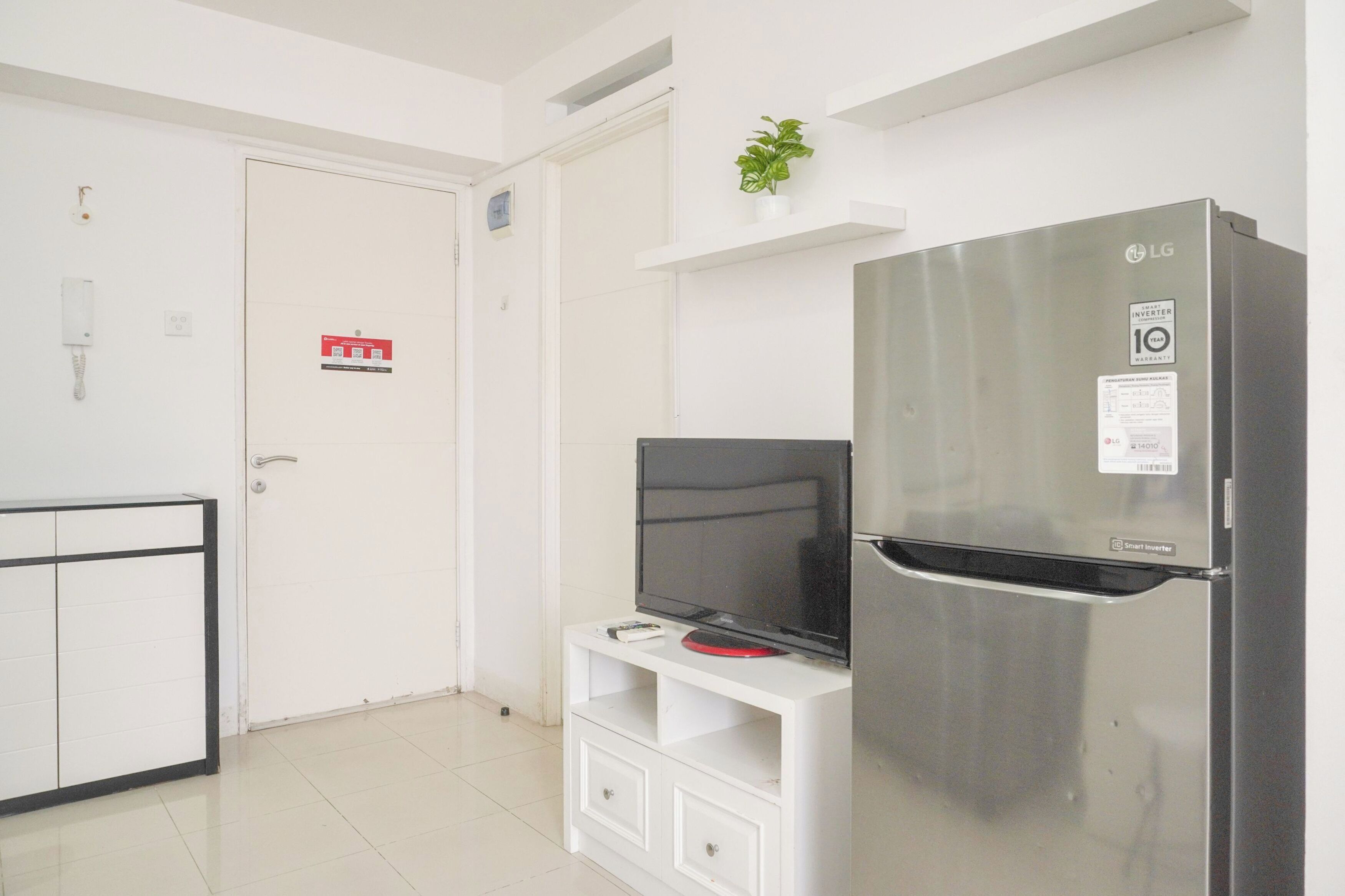 A modern kitchen with a stainless steel refrigerator, a white cabinet, and a flat-screen TV on a white stand.