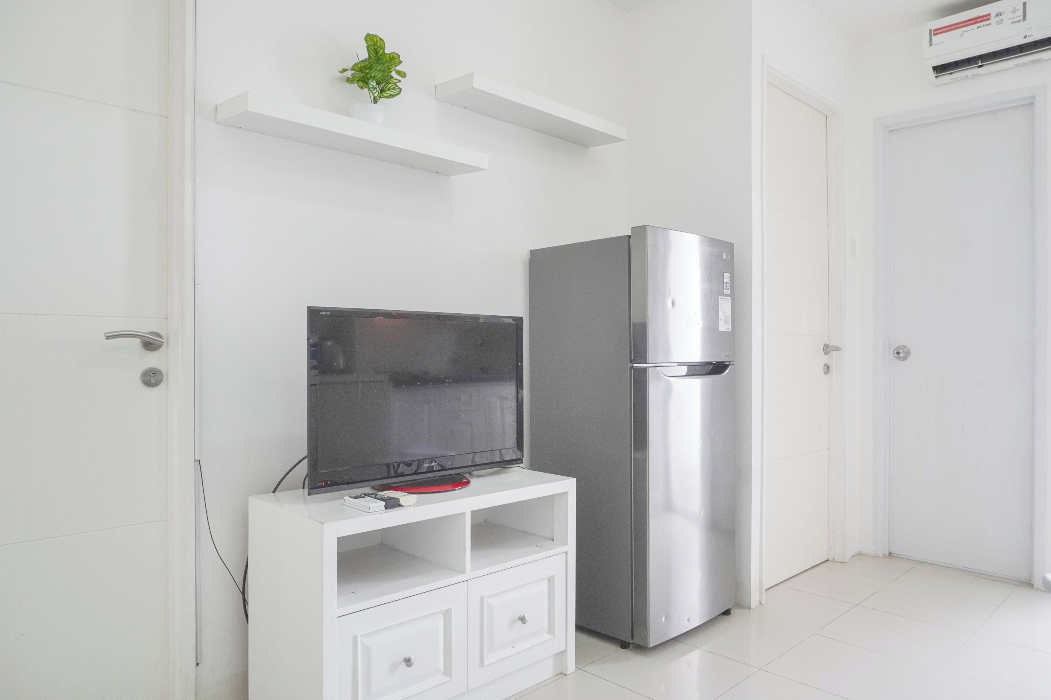 A modern kitchen with a built-in refrigerator, a flat-screen TV on a white cabinet, and a small plant on a shelf.