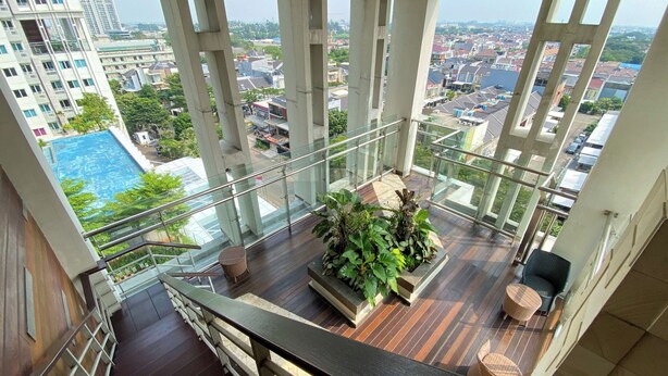 Un edificio alto con balcón de cristal que da a una vista panorámica de la ciudad y una piscina.