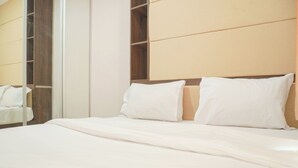 Una cama bien hecha con sábanas y almohadas blancas, un cabecero de madera y un espejo grande en la pared.