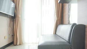Una sala moderna con un sofá, un televisor de pantalla plana montado en la pared y cortinas translúcidas.
