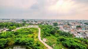A panoramic view of a city with a mix of greenery and urban buildings, a winding path, and a body of water in the foreground.