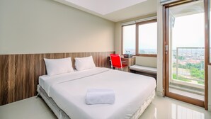 A hotel room with a large bed, a wooden headboard, a red chair, a desk, and a large window with a city view.