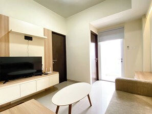 Uma sala de estar moderna com televisão de tela plana, armários de madeira, uma mesa branca e um sofá bege.
