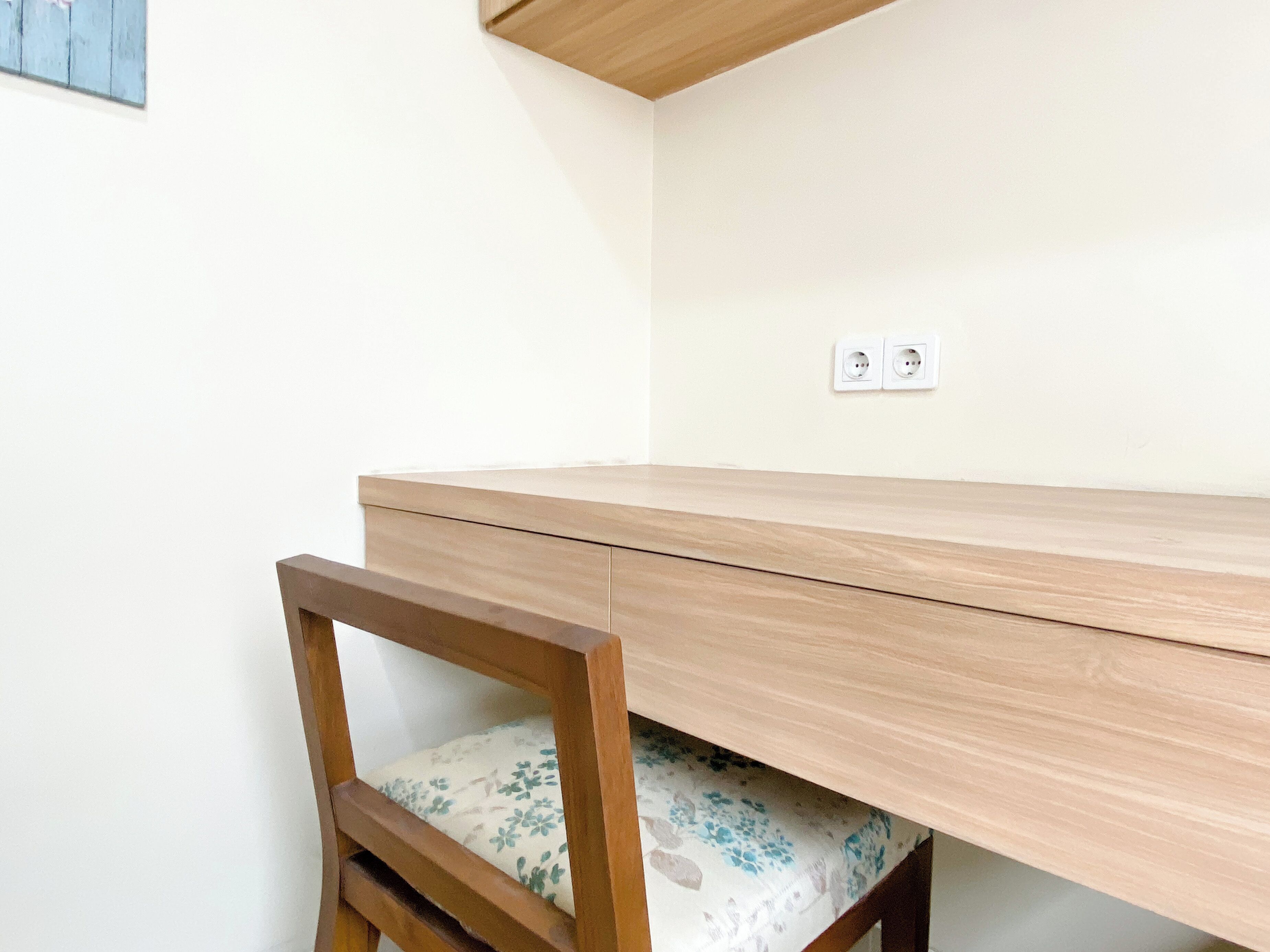 A wooden desk with a chair underneath, a white wall, and two electrical outlets.