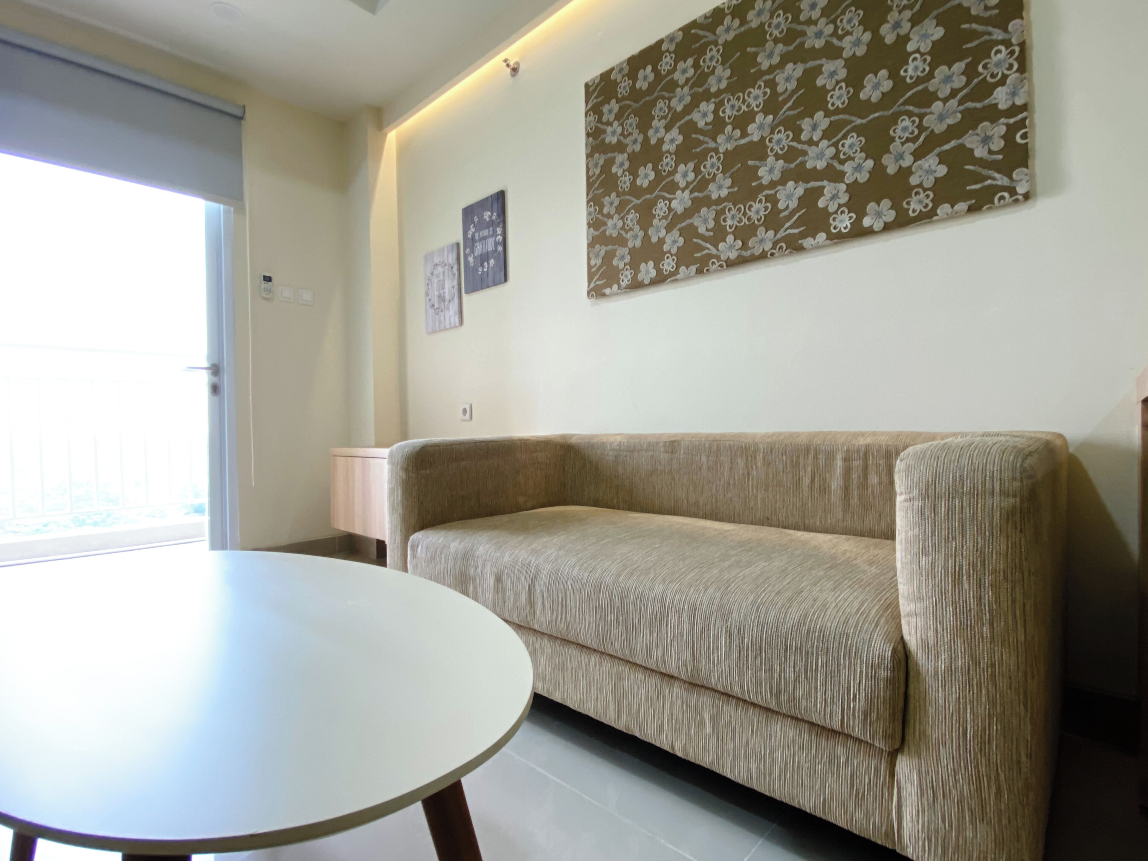 A living room with a beige sofa, a round table, and a wall with floral artwork.