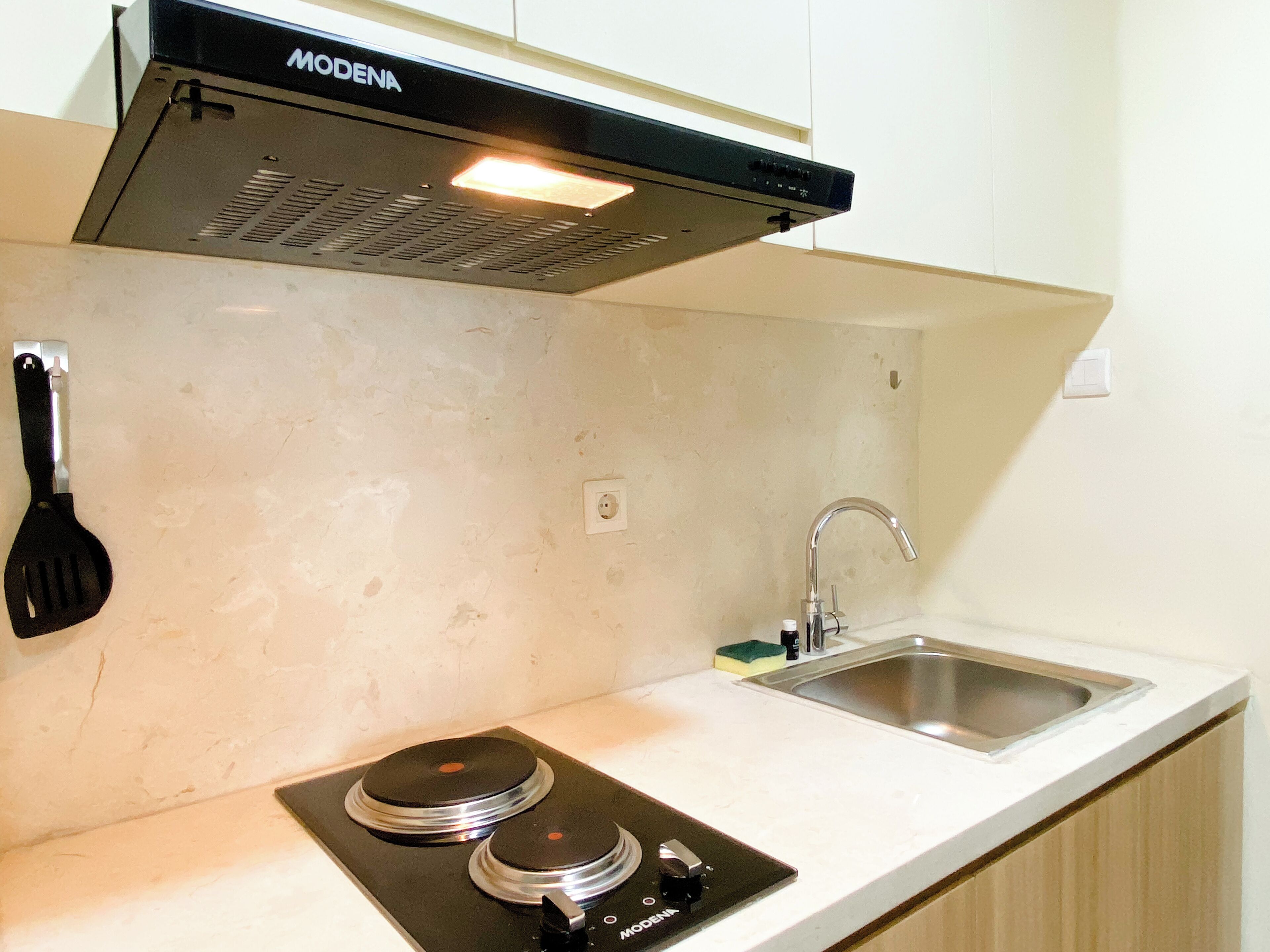 A kitchen with a stove, sink, and a spatula hanging on the wall.