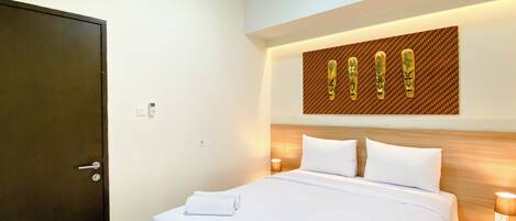 A hotel room with a bed, a wooden headboard, a wall-mounted artwork, a bedside table with a lamp, and a door.